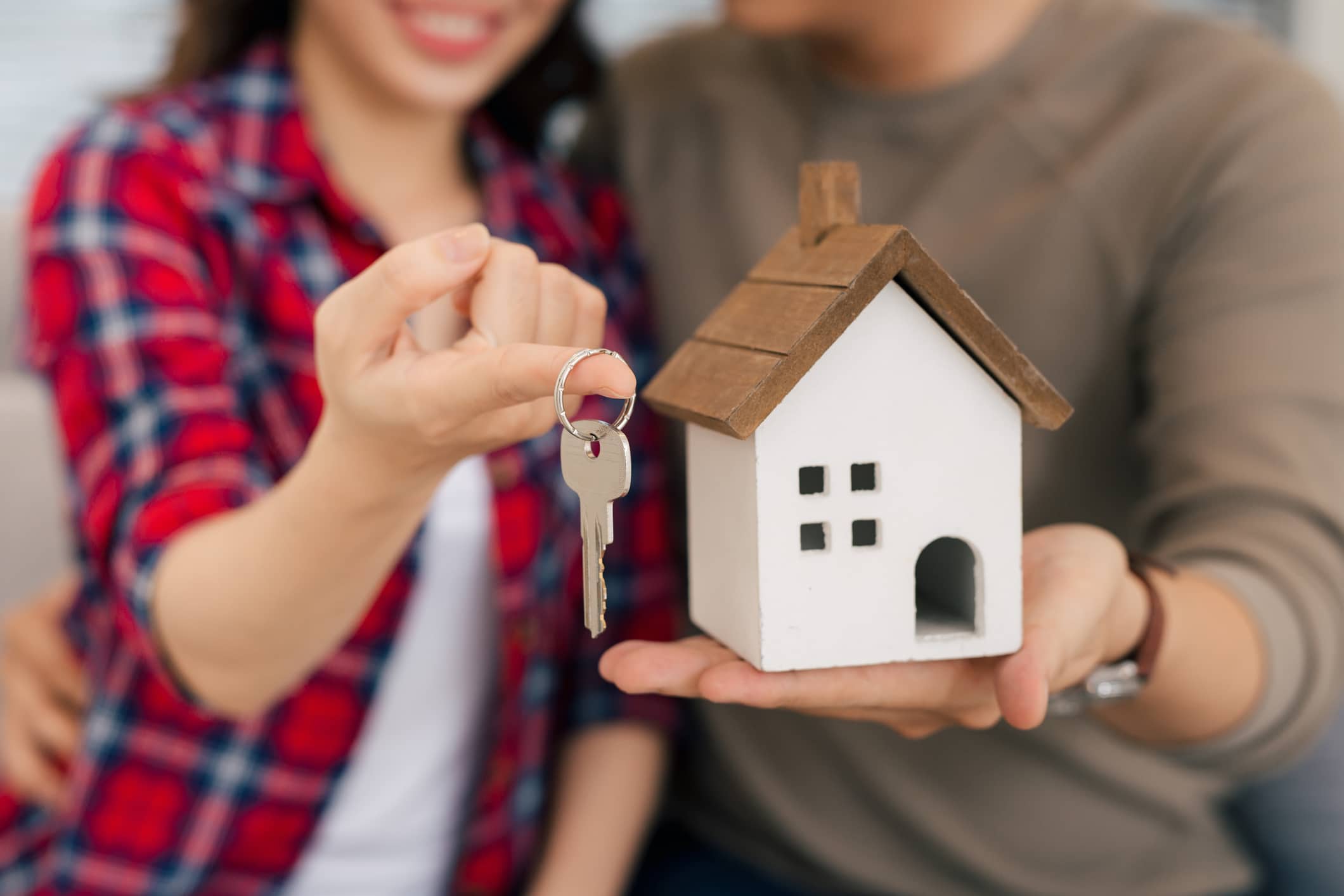 Proud couple holding keys and wooden house figurine